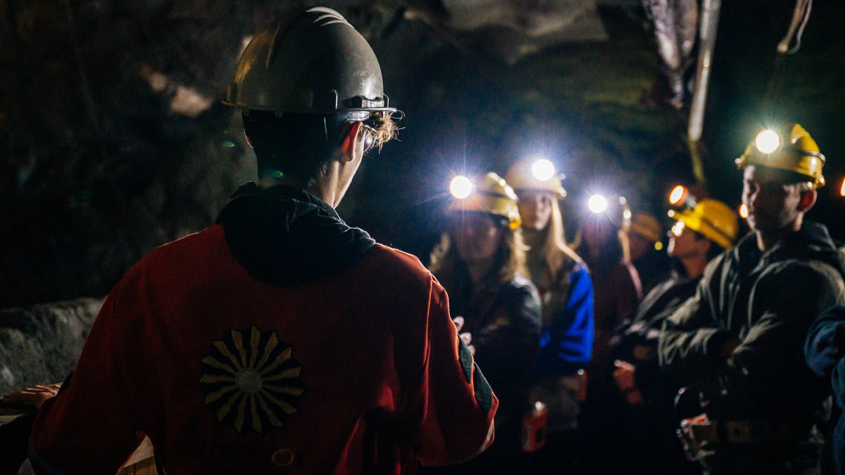 Group of people in a dark mine, wearing safety helmets.