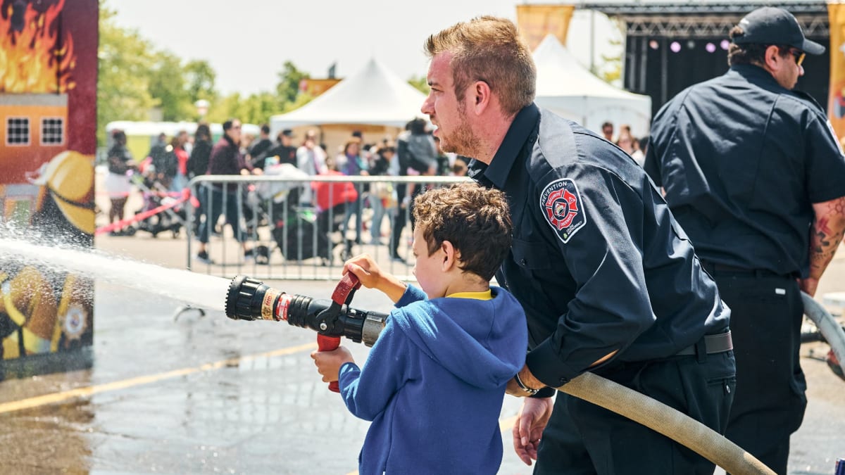 Firefighter showing a boy how to use the hose.