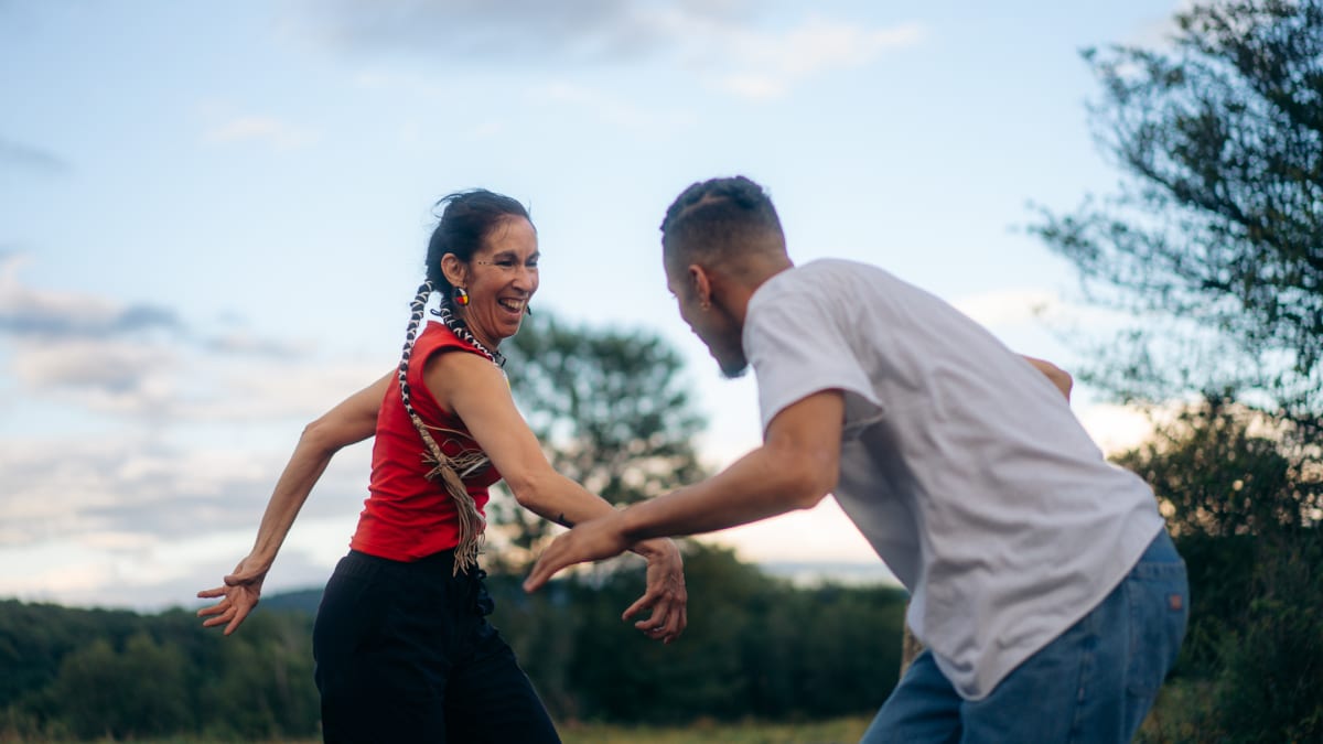 An Indigenous woman and a man have fun dancing outdoors