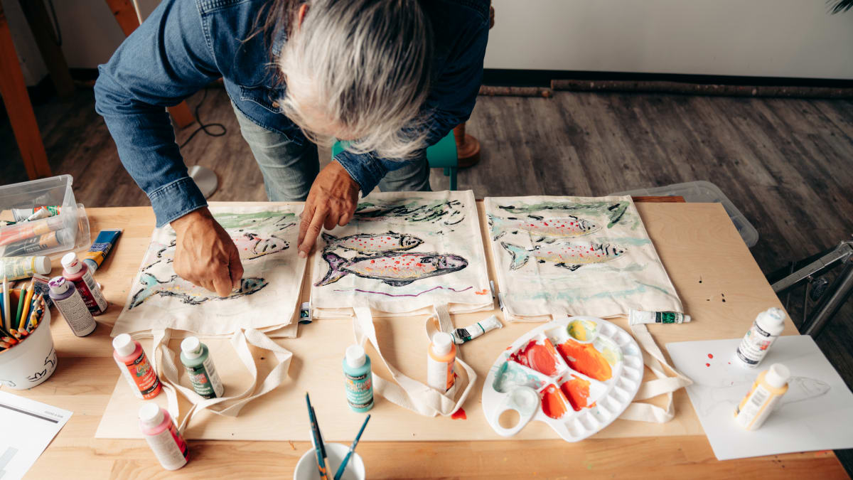 An Indigenous woman paints fish on a cloth