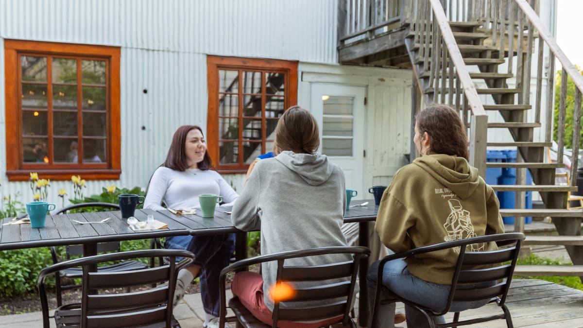 Terrasse extérieure de l’Auberge Internationale de Rivière-du-Loup, où trois personnes sont assises à une table près d’un feu.