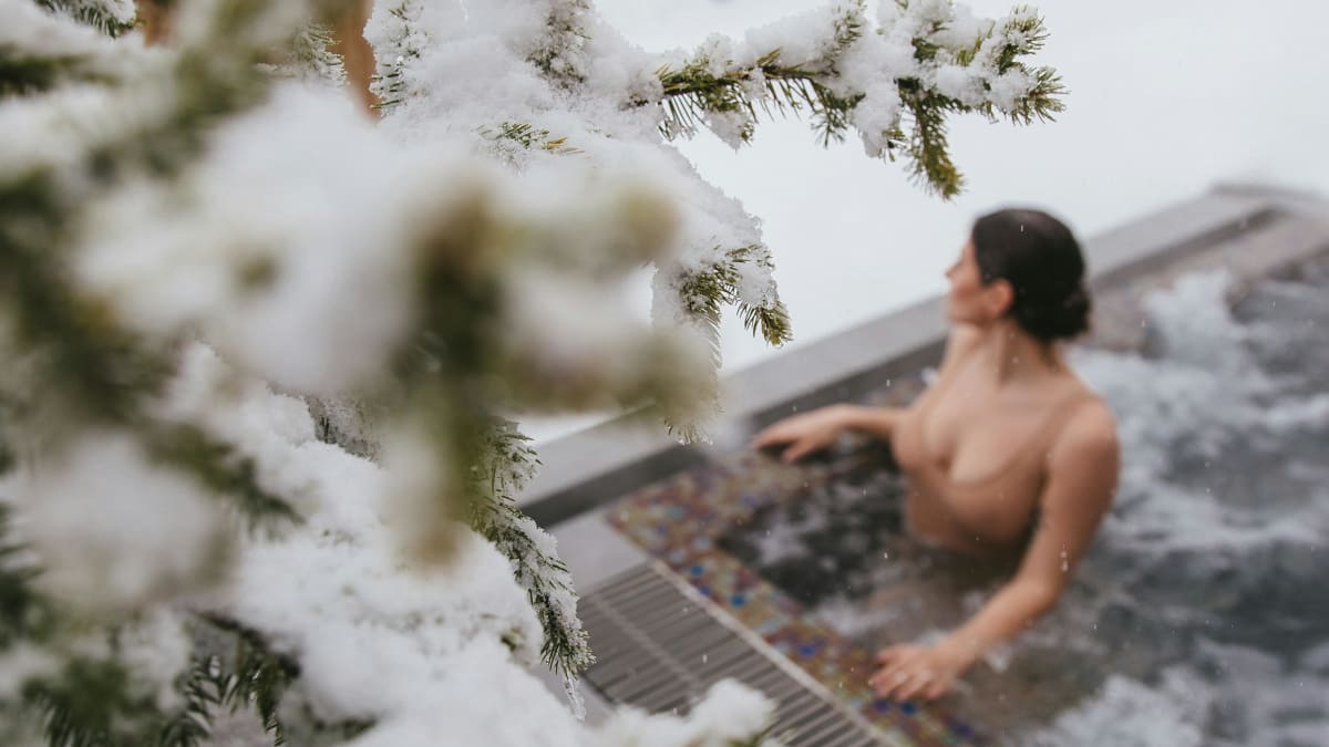 Woman in an outdoor spa; around her, there are snow-covered trees.