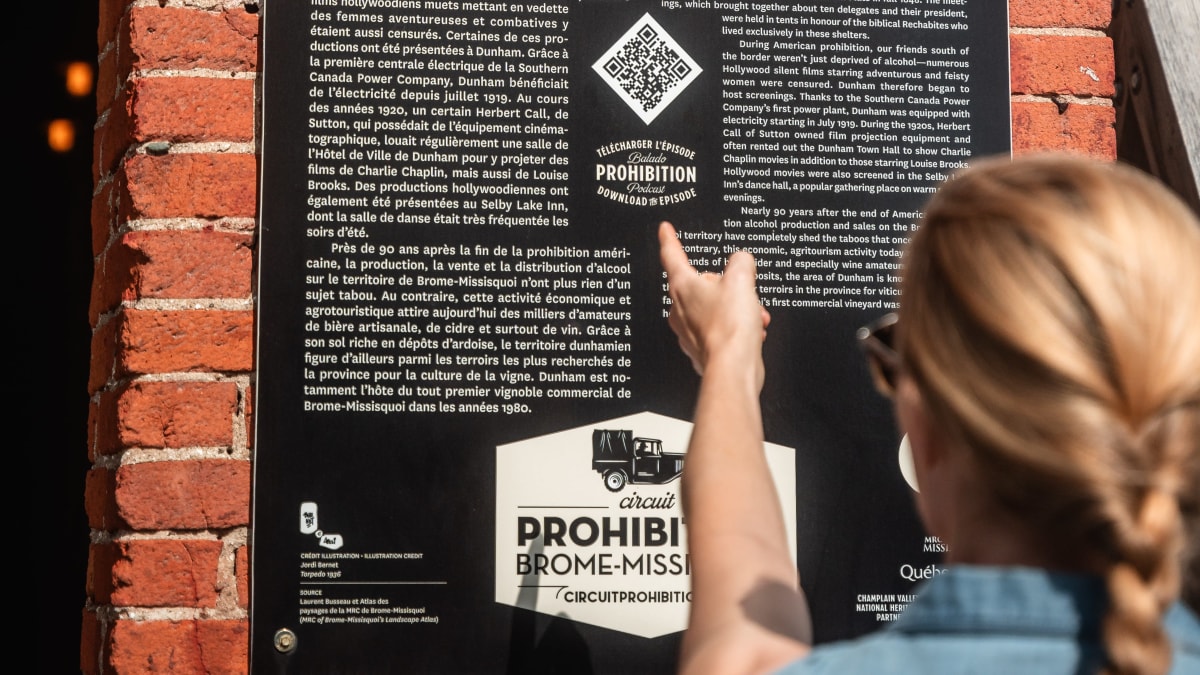 Femme en train de lire une affiche à l'effigie du Circuit de la Prohibition.