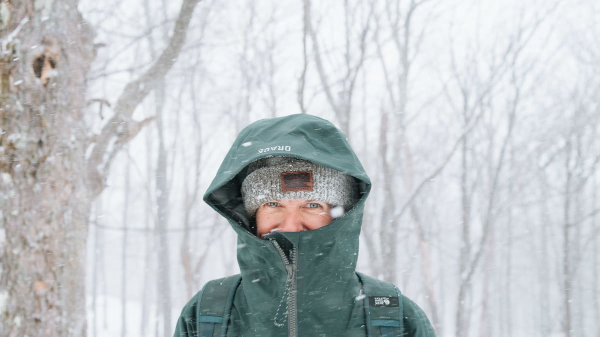 Woman wrapped up in a green coat in the middle of a snowy landscape.