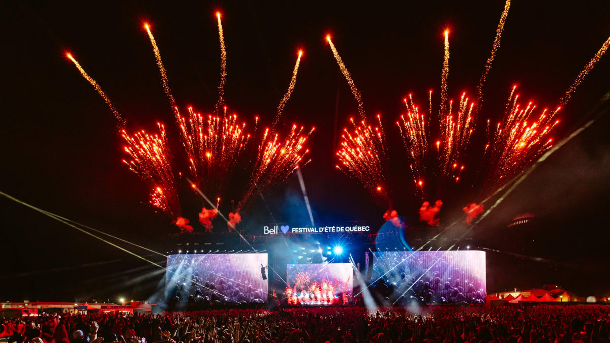 Crowd in front of an outdoor stage at night with fireworks.