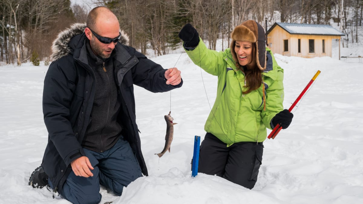 Couple ice fishing, the man has a fish at the end of his line.