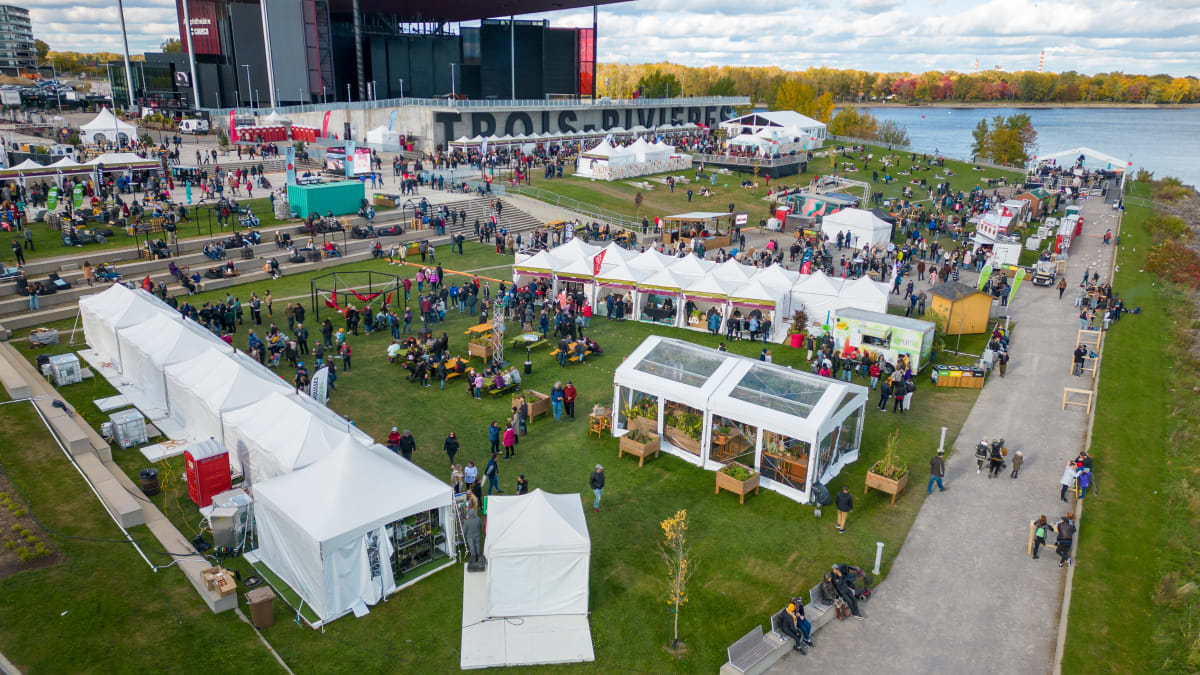 The Amphithéatre Cogeco in Trois-Rivières by the river, with kiosks and spectators on the grass.