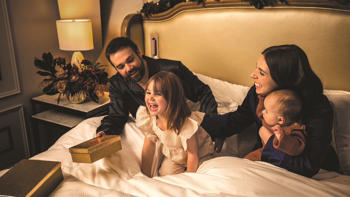 Two parents with a young daughter and a baby in a luxurious hotel bed.