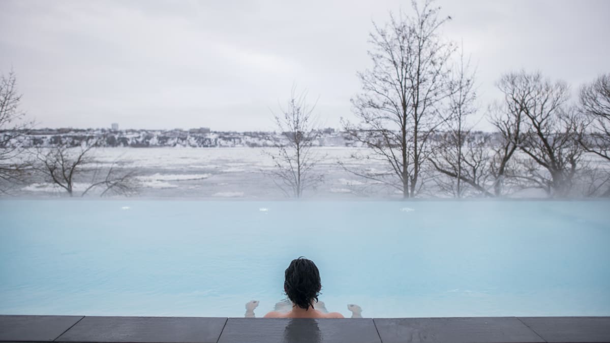 Person in a spa seen from behind as they look out over the St. Lawrence River in winter.