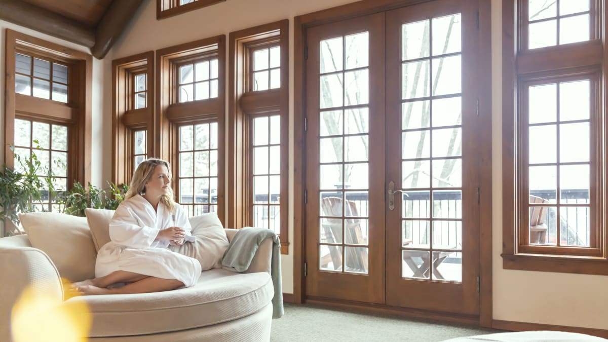 Woman in bathrobe sitting on a comfy chair in a room with many windows.