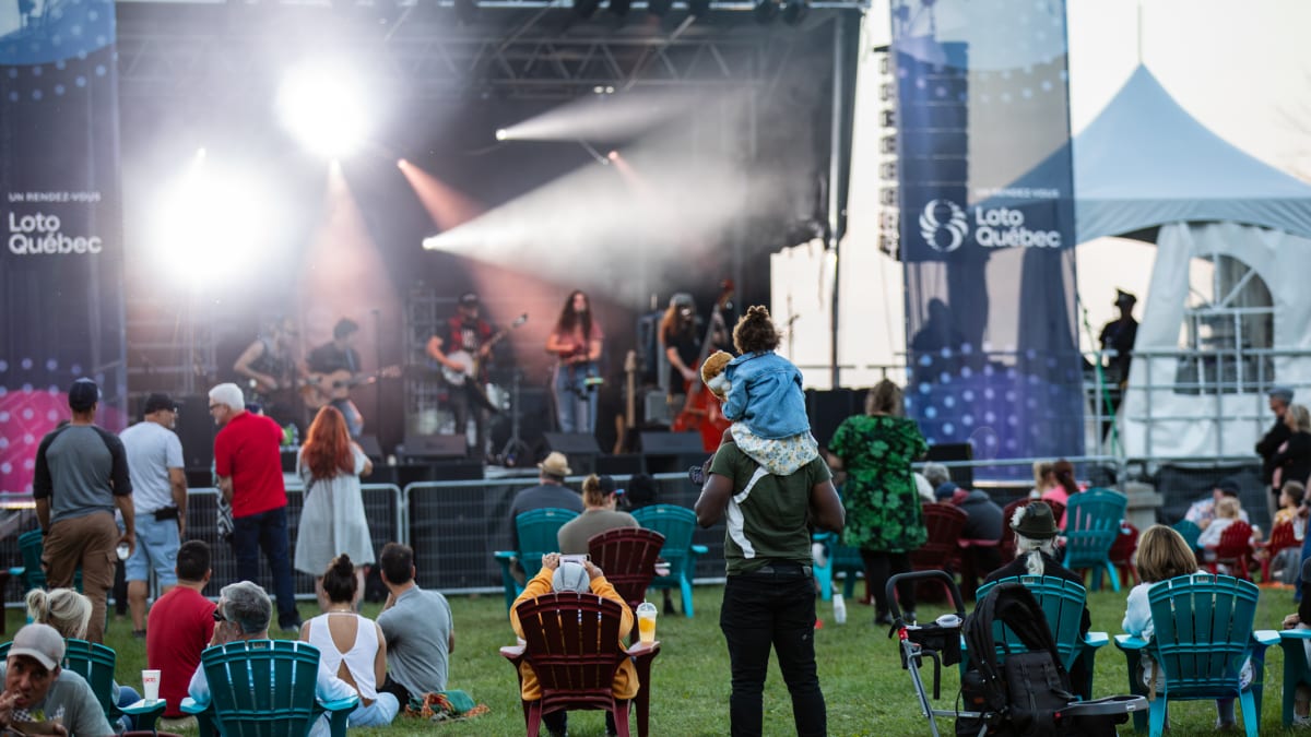 Festival grounds in front of a stage, with chairs and families.