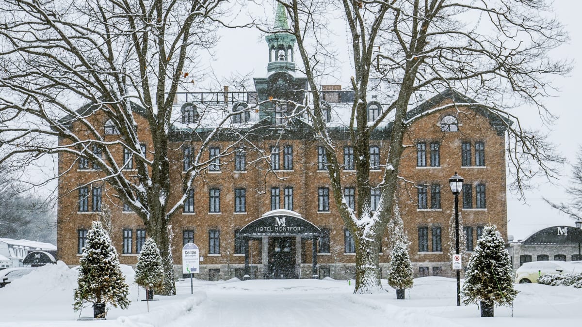 Front of the Hôtel Montfort, a historic 4-storey building, under falling snow.