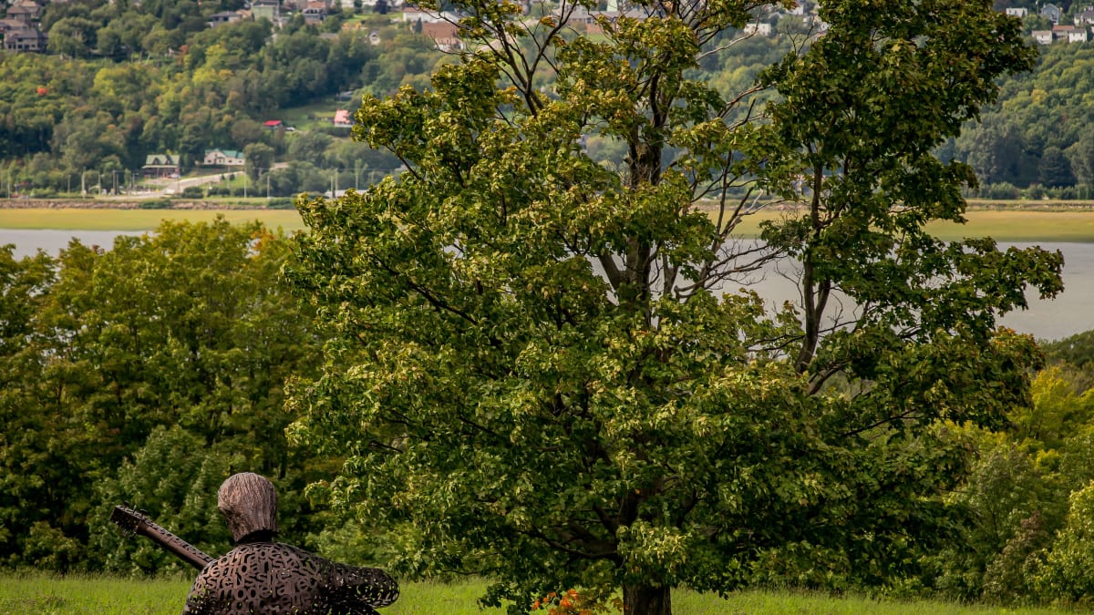Sculpture représentant Félix Leclerc et paysage côtier de l'ile d'orléans.