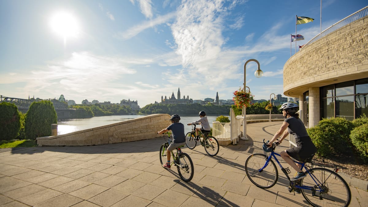 Mère et deux fils en vélo à côté du Musée canadien de l'histoire face à la rivière des Outaouais.