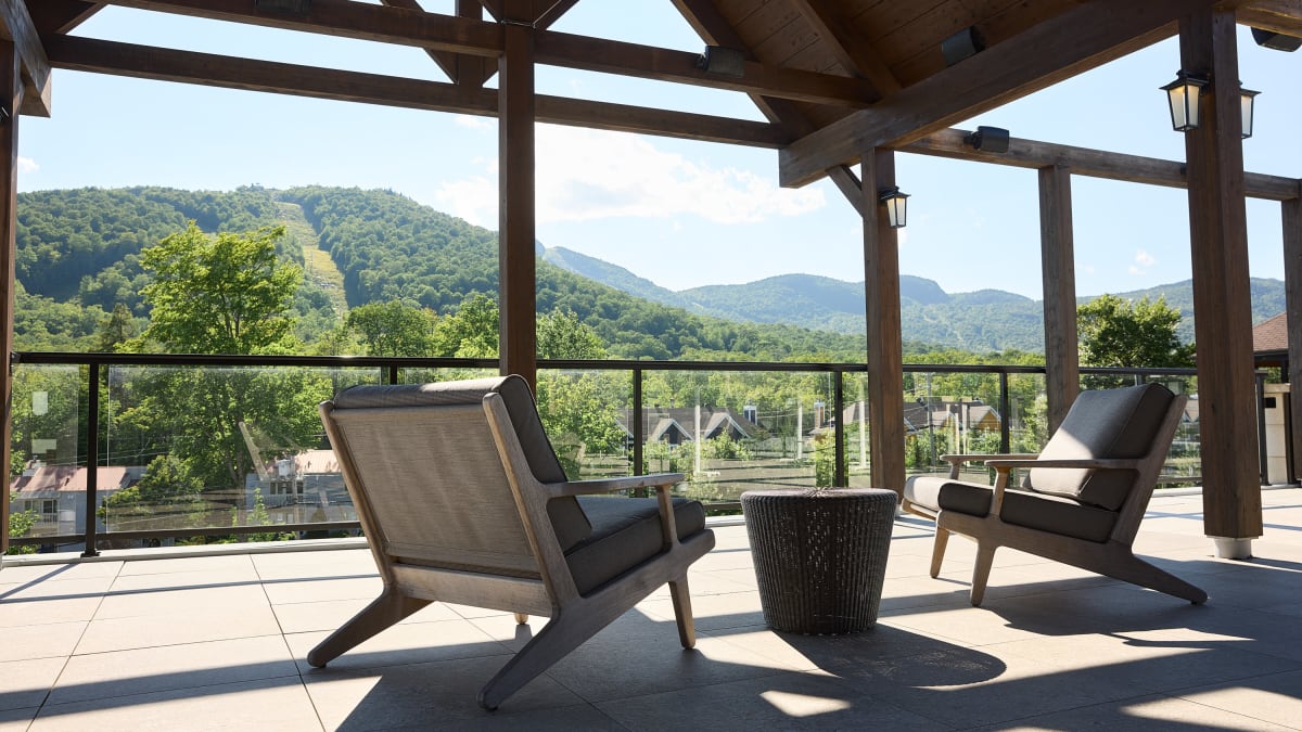 A covered outdoor terrace, featuring two comfortable chairs, overlooks a mountainous landscape.