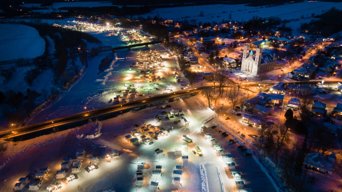 Lit-up ice fishing village seen from above at night.