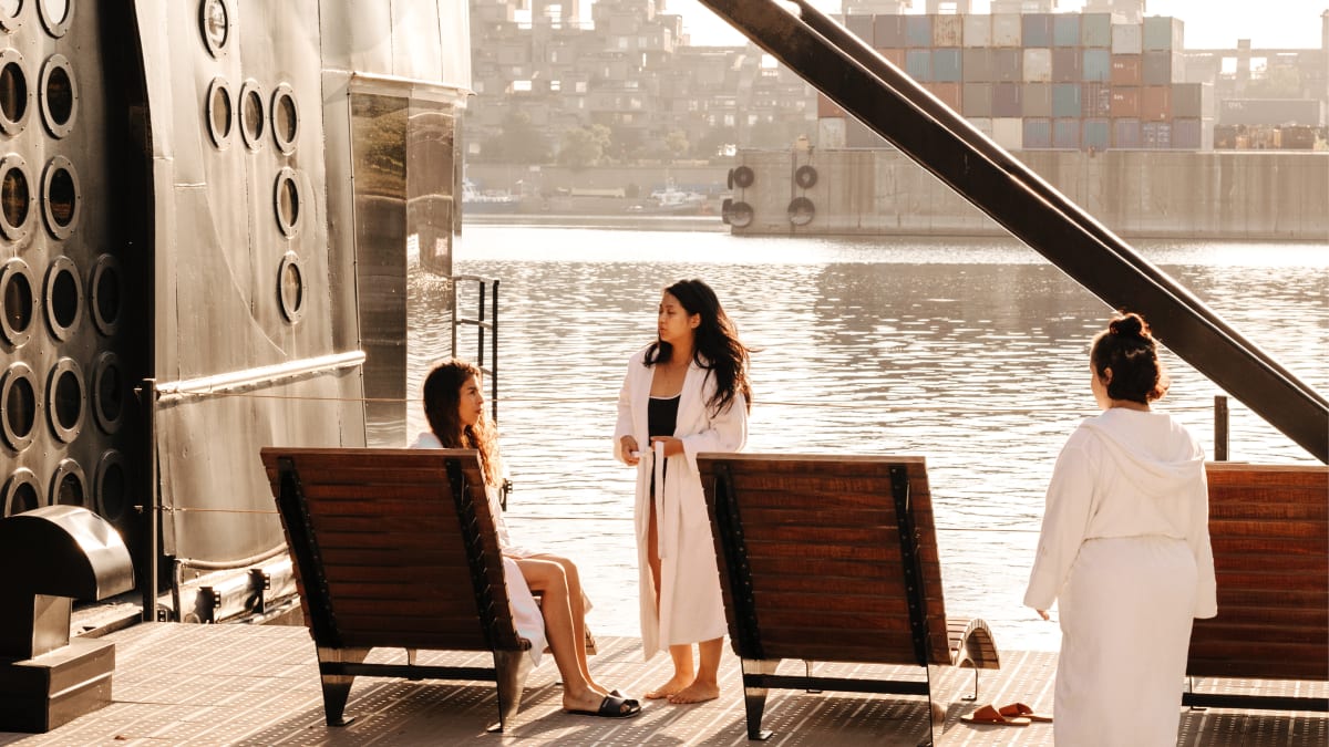 Three women in bathrobes on the spa terrace overlooking the water.