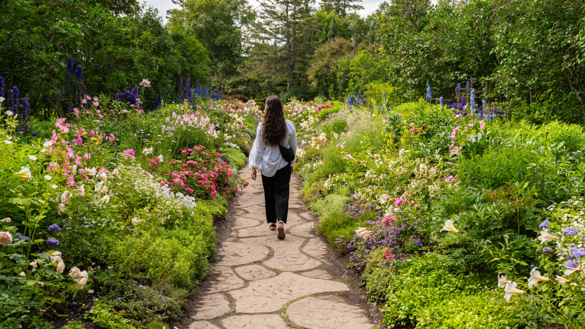Woman walking on a stone path through a flower garden.