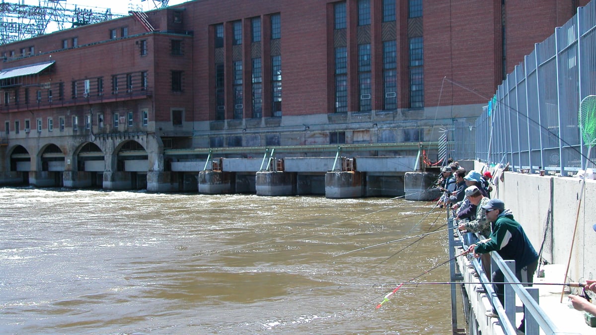 A row of fishermen fishing from the top of a dam.