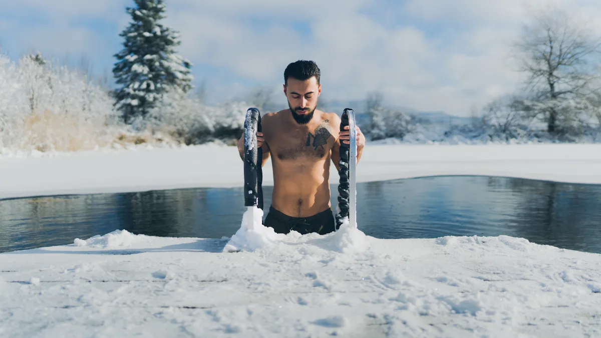 A man emerging from a pool of water surrounded by snow.