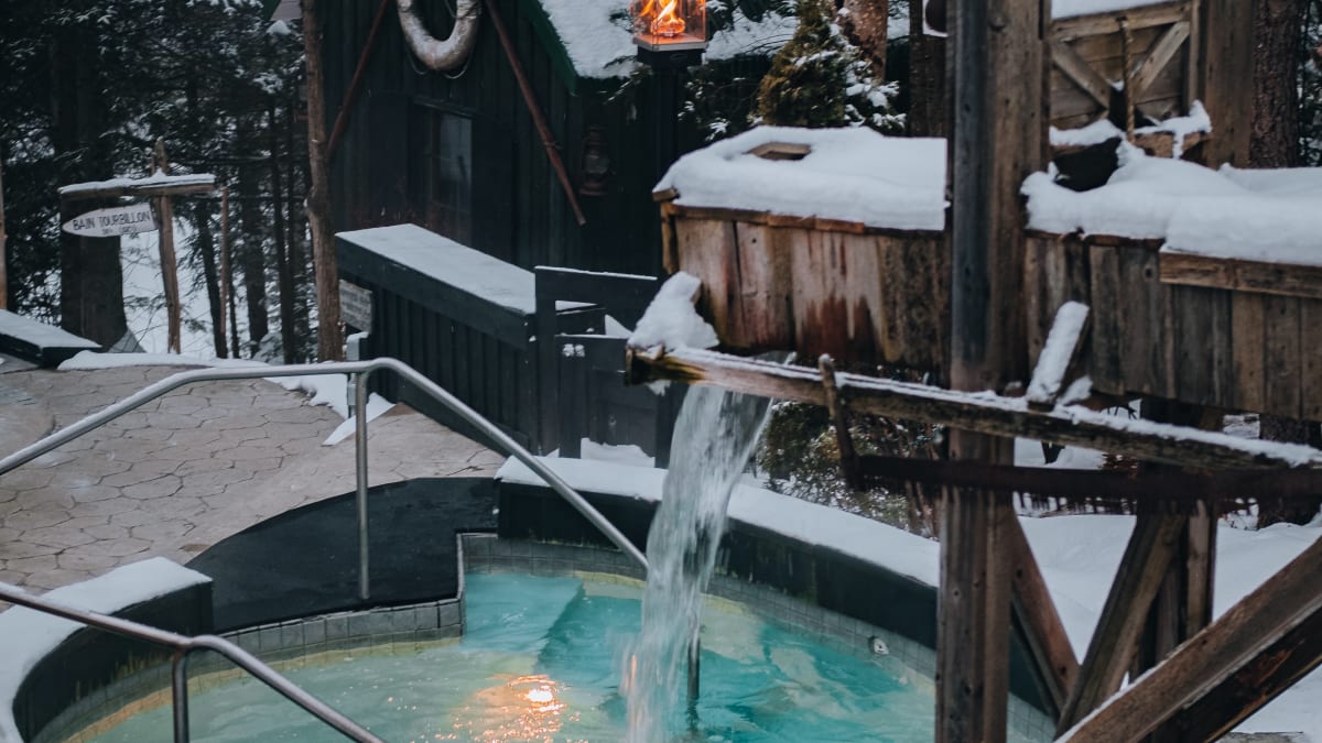 A thermal pool surrounded by snow and trees at dusk.