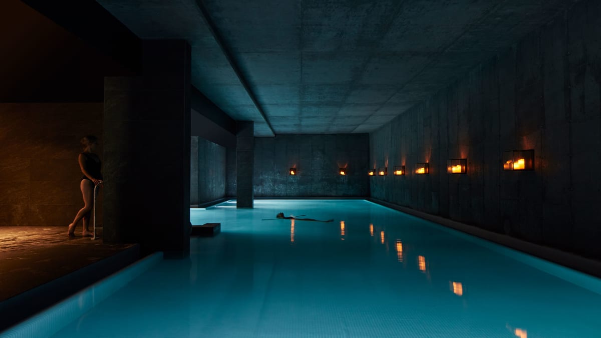 Piscine intérieure dans la pénombre, éclairée par une douce lumière; une femme se tient au bord de la piscine.