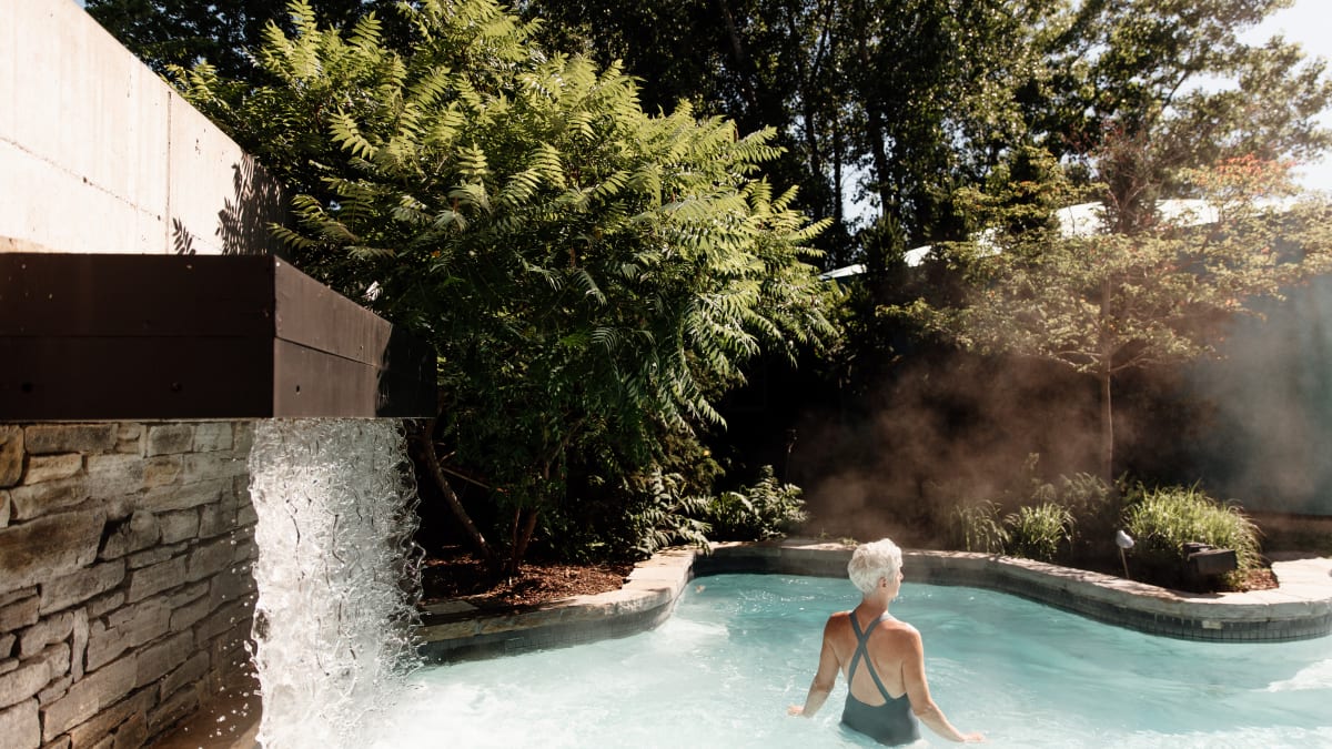 Femme dans un bain extérieur du spa; une chute d'eau alimente le bain.