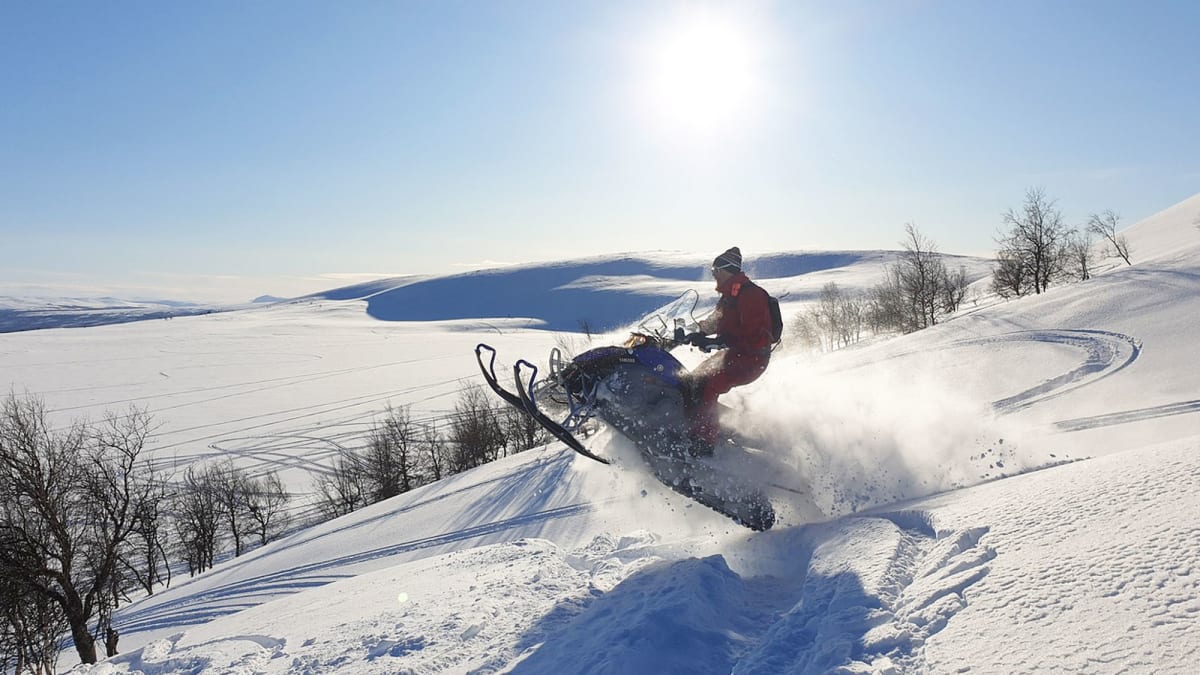Person snowmobiling through a vast snow-covered landscape.