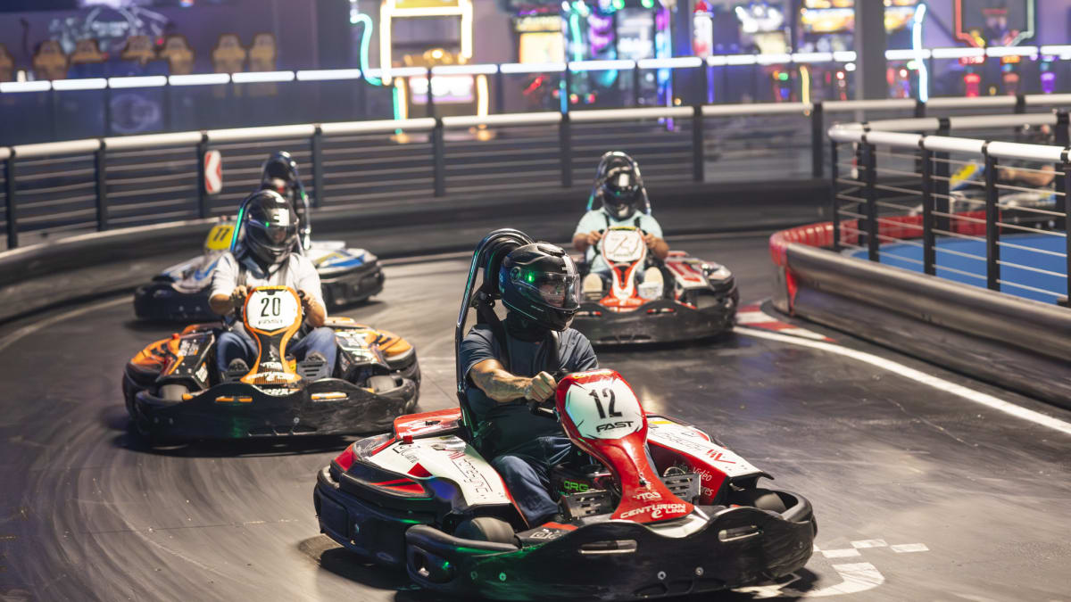 Four people in a go-kart on a karting track.