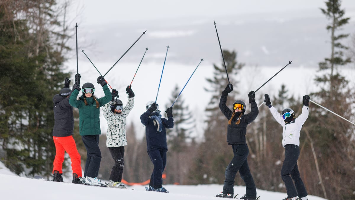 6 skieurs et skieuses en haut de la montagne qui soulèvent triomphalement leurs bâtons.