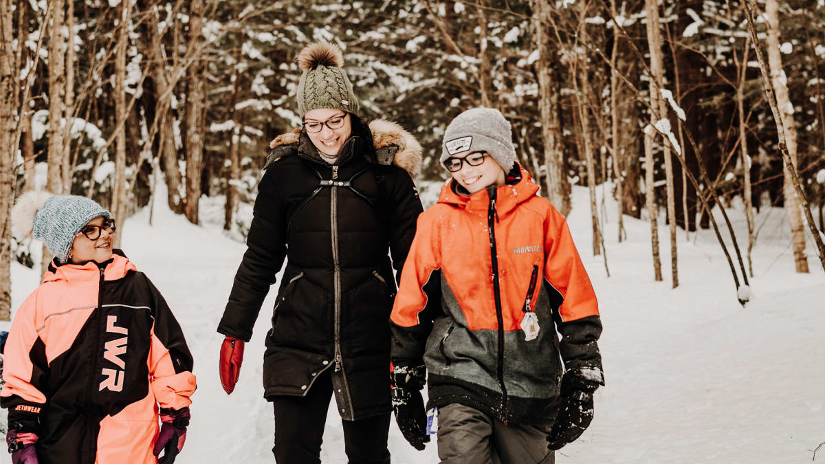 A mother and two children, all smiling, in a snowy forest.