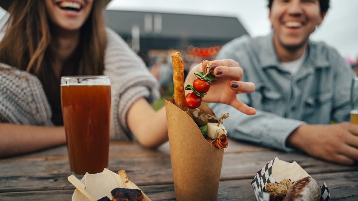 An assortment of food on a table in the foreground, with two happy-looking people sitting at the back.