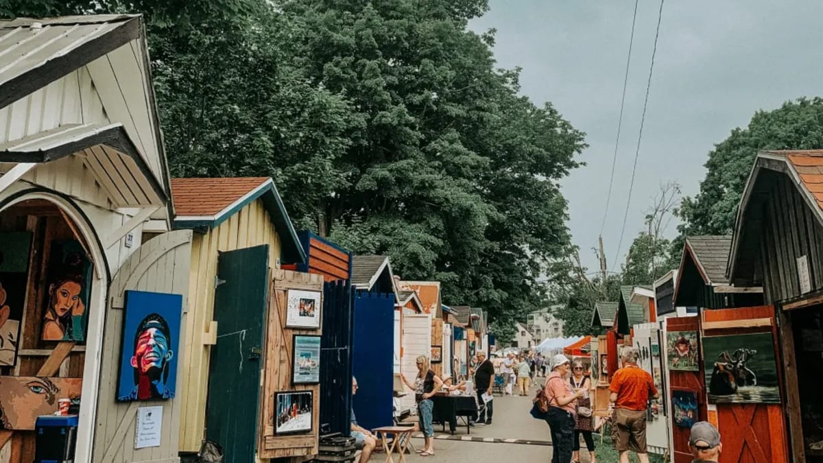 An alleyway lined with small cabins showcasing works of art.