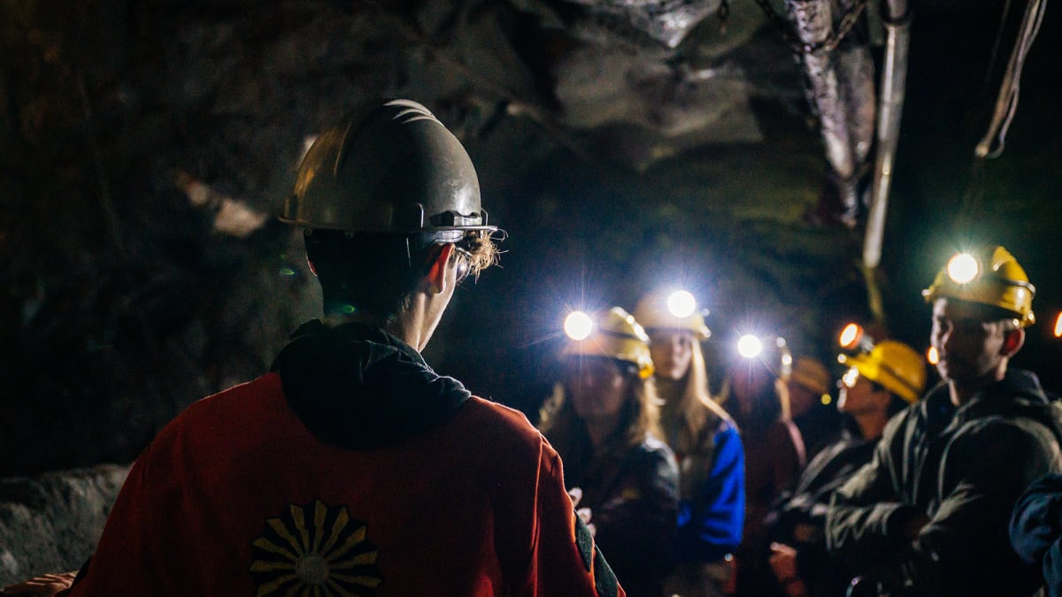 Group of people in a dark mine, wearing safety helmets.