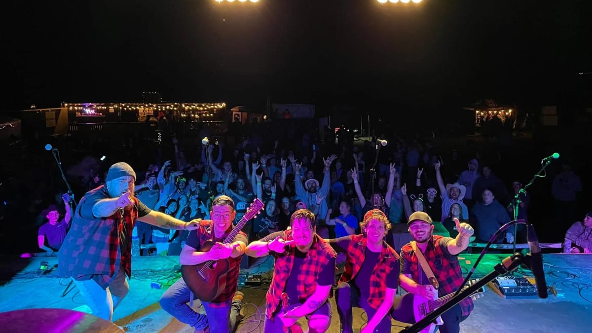 A group of musicians on stage being photographed in front of the crowd at a festival.
