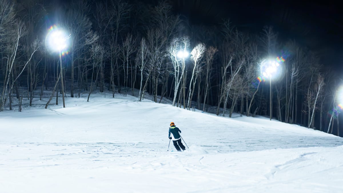 Personne seule en train faire du ski alpin en soirée sur une piste éclairée.