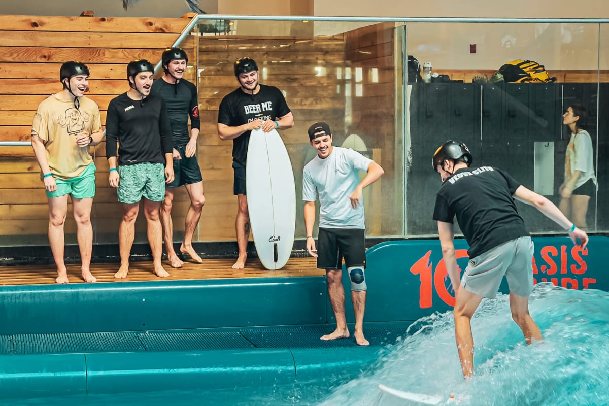 Man surfing in an indoor pool, with a group of people watching