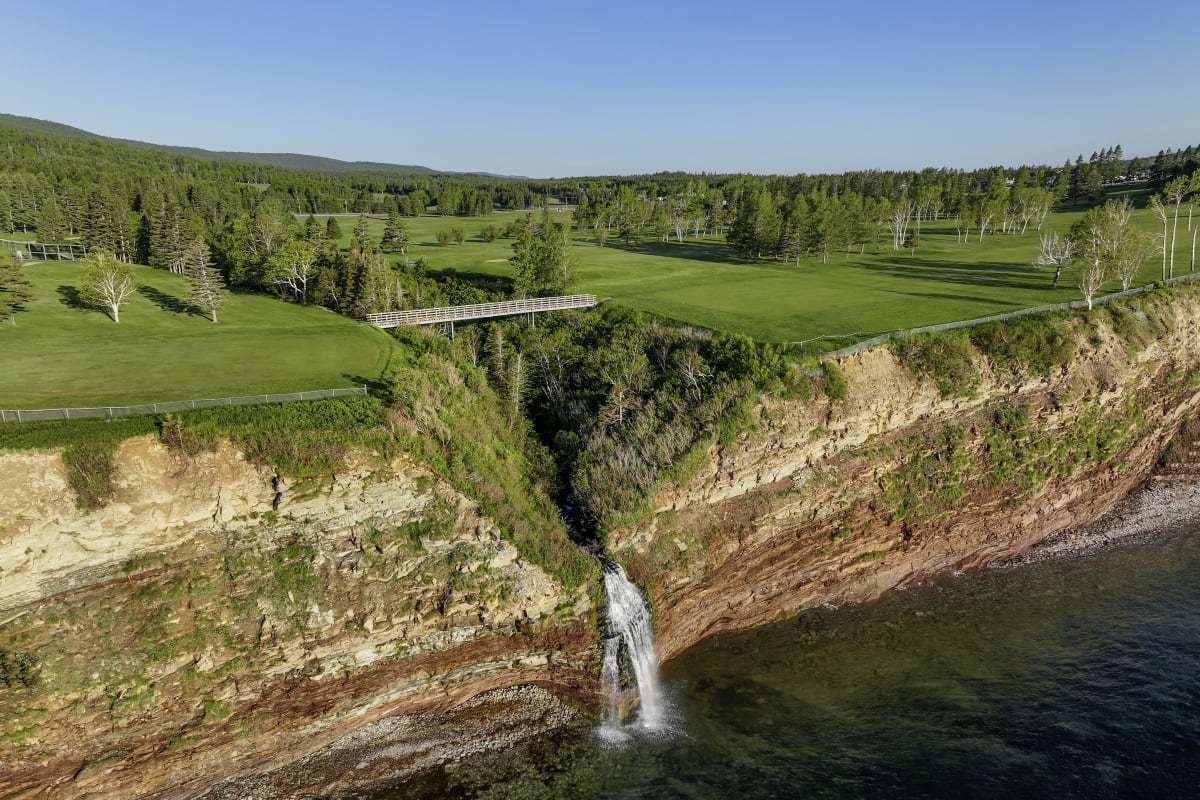 At the edge of a lush green golf course, a body of water meets a reddish cliff. 