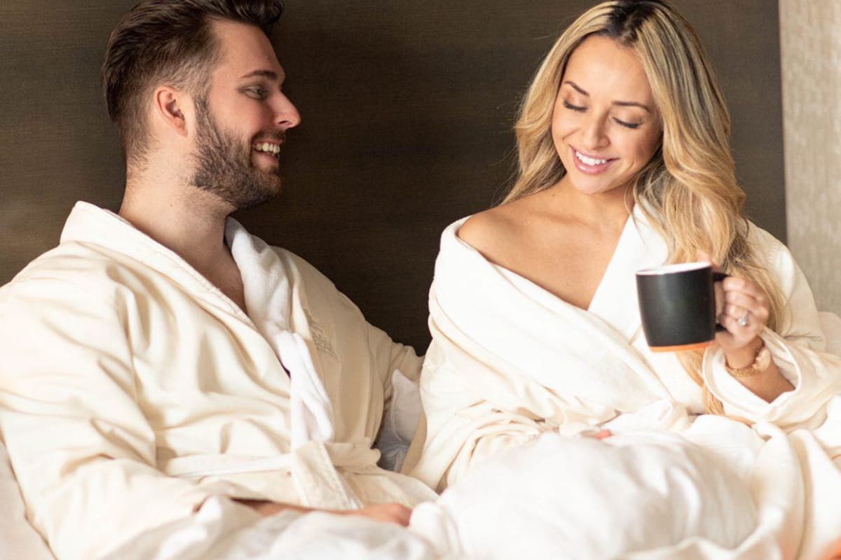 Couple relaxing in bed wearing bathrobes and enjoying a cup of coffee.
