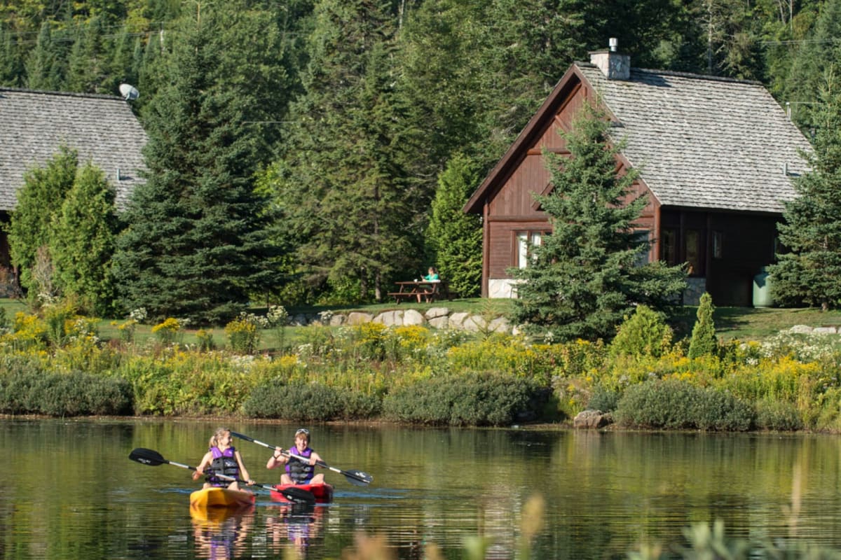 Two people in a kayak on a body of water in front of one of the Chalets Royal Laurentien.