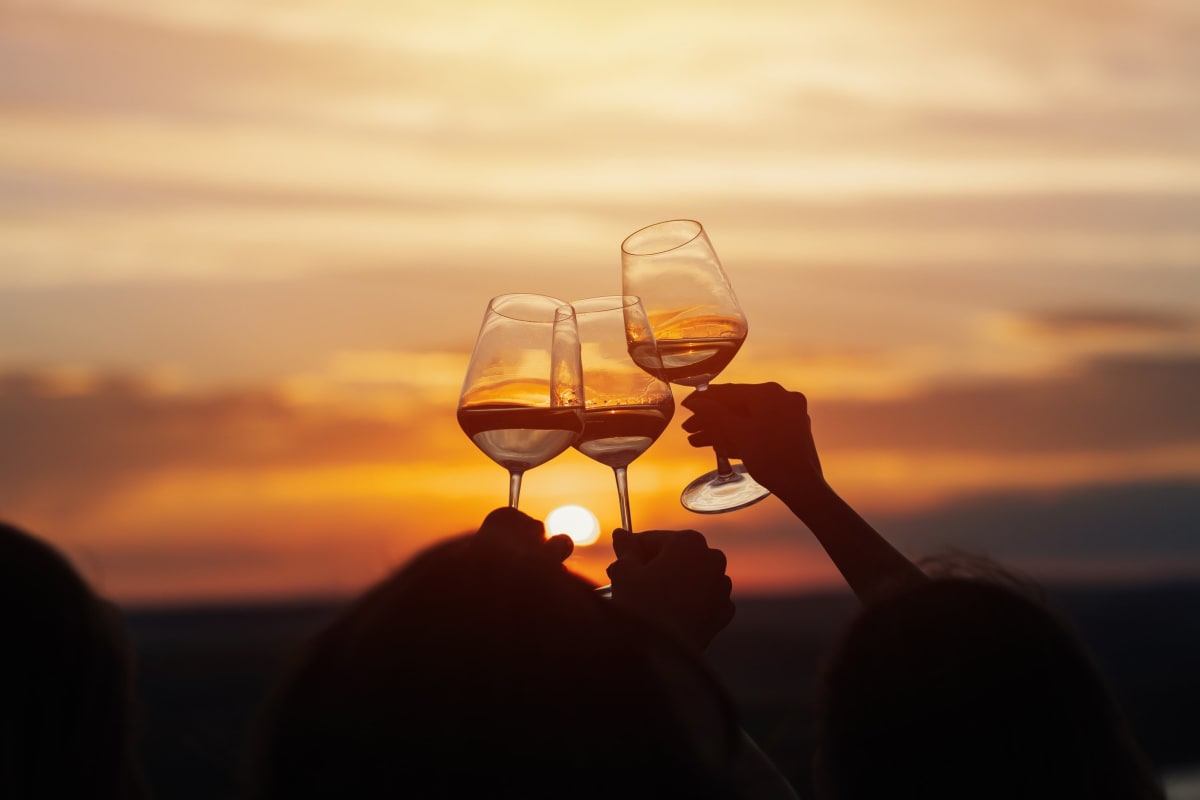 Three glasses of wine raised before a sunset