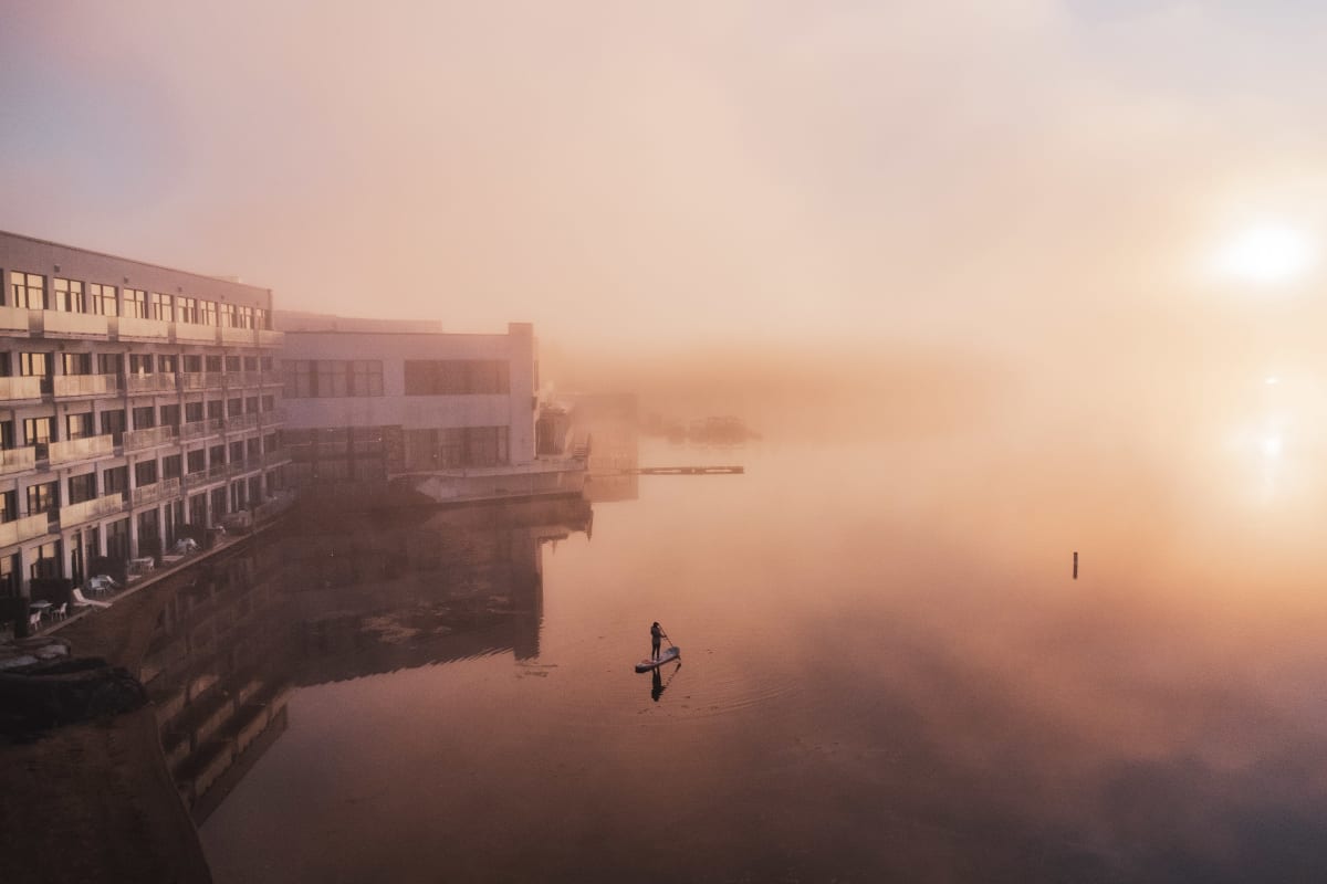 Aerial view of a woman stand-up paddleboarding on the lake at dawn.