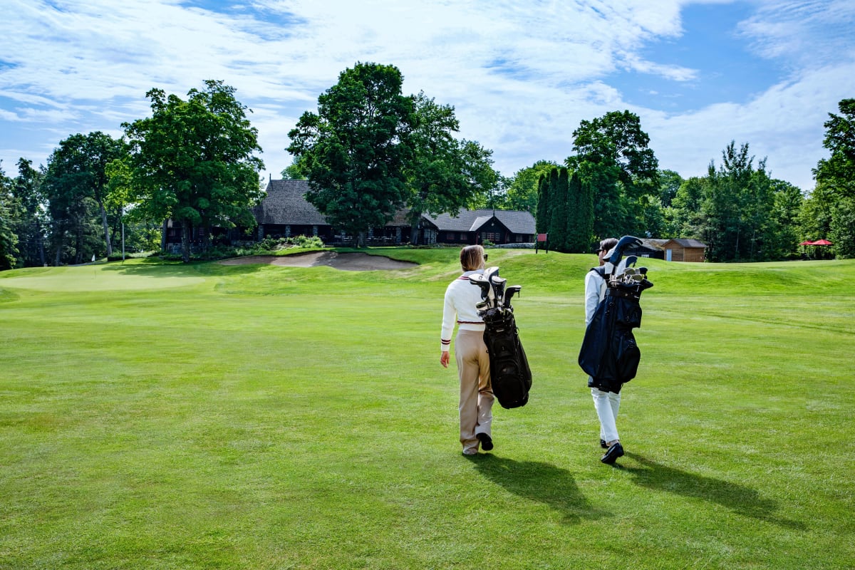 Deux personnes sur un terrain de golf qui portent leur sac sur le dos.