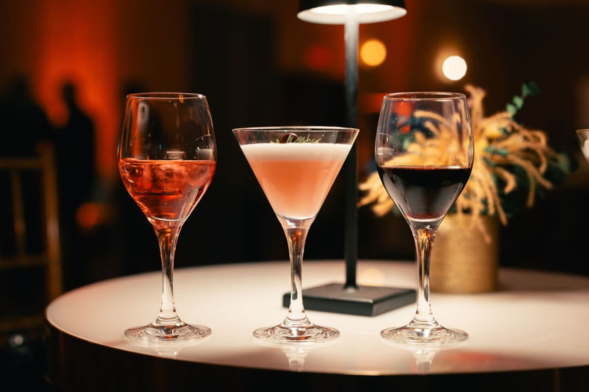 Deux verres à vin et un verre à martini alignés sur une table sous une lumière tamisée.