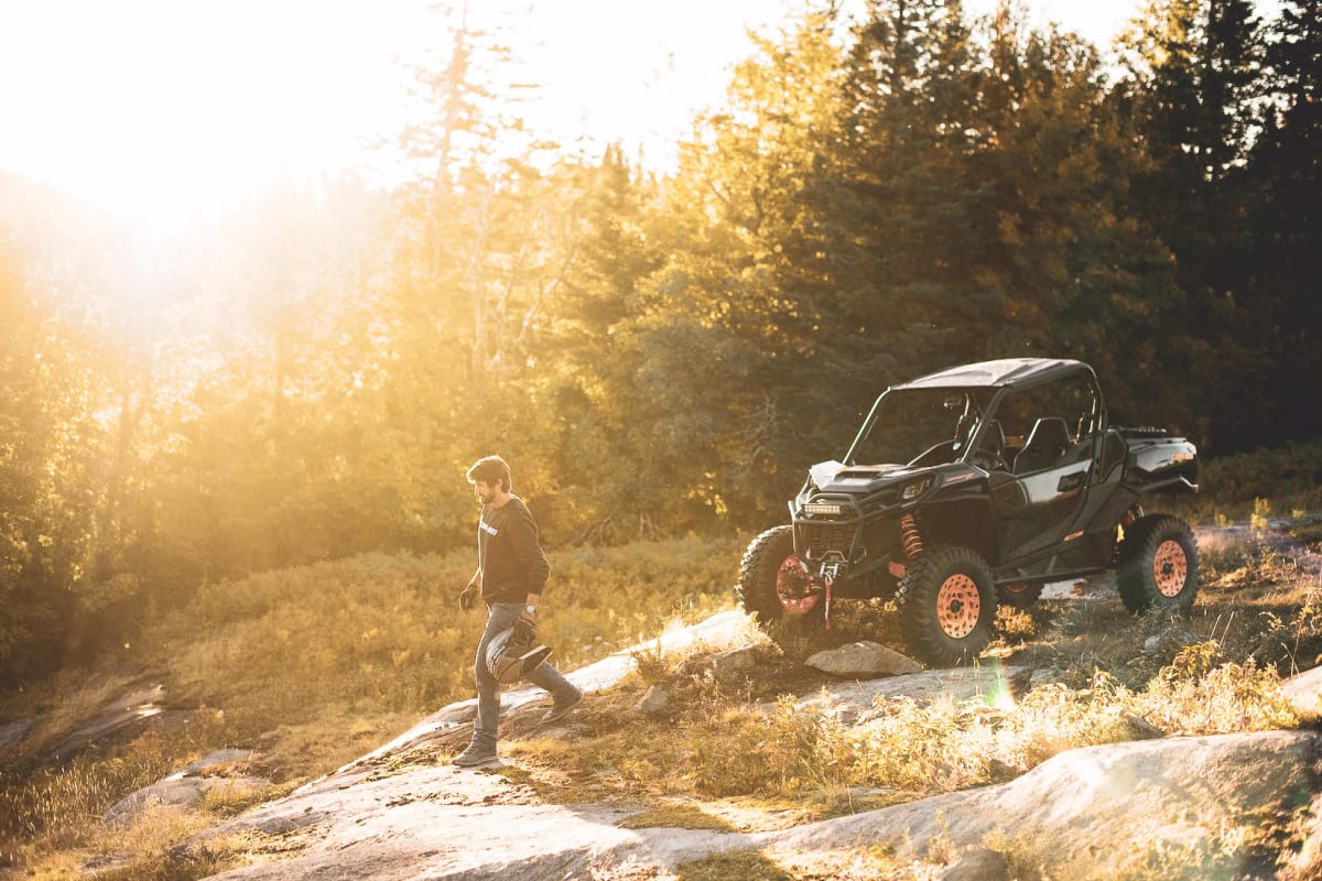 A person standing next to an ATV in nature, with the sun shining brightly.