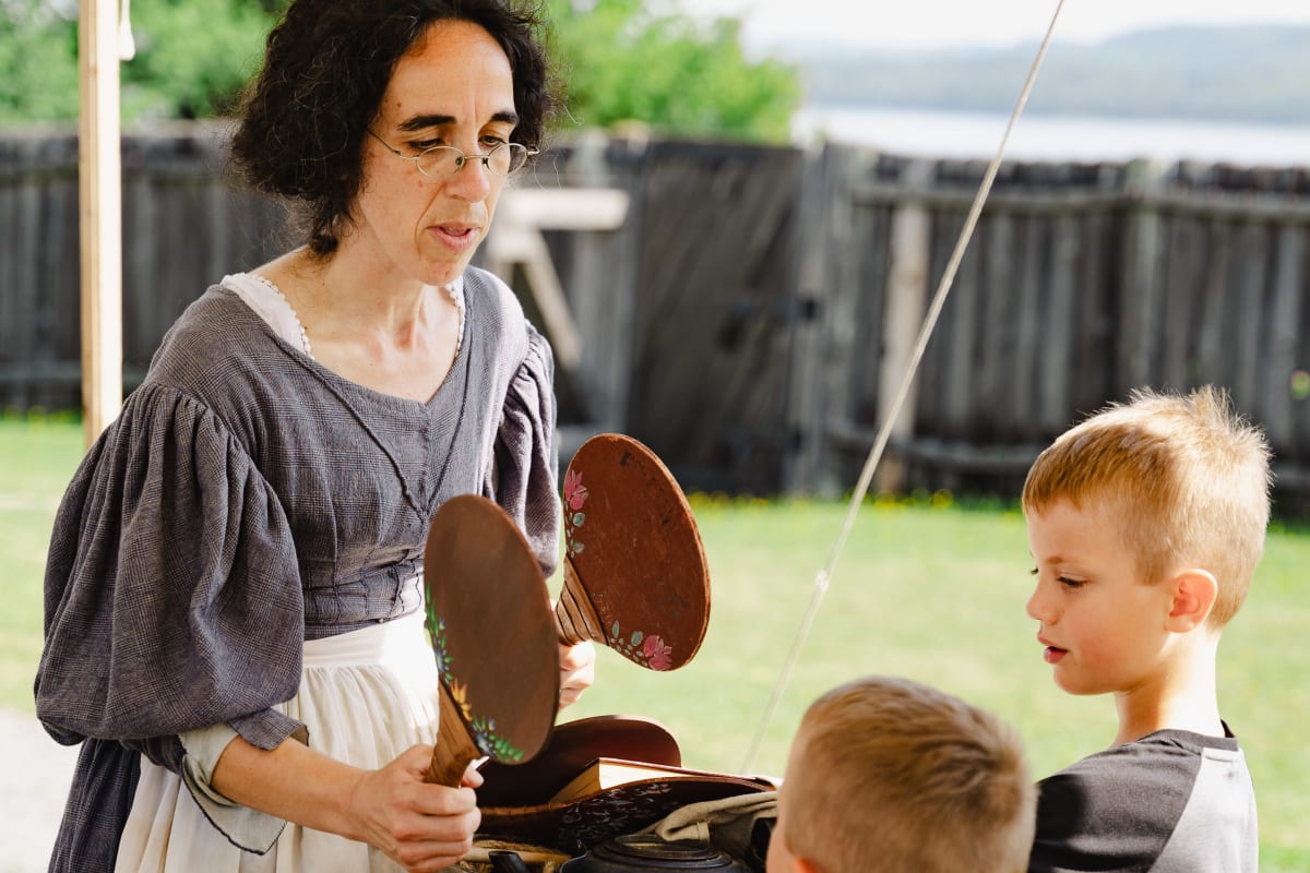 A woman in period costume interacting with two young boys.