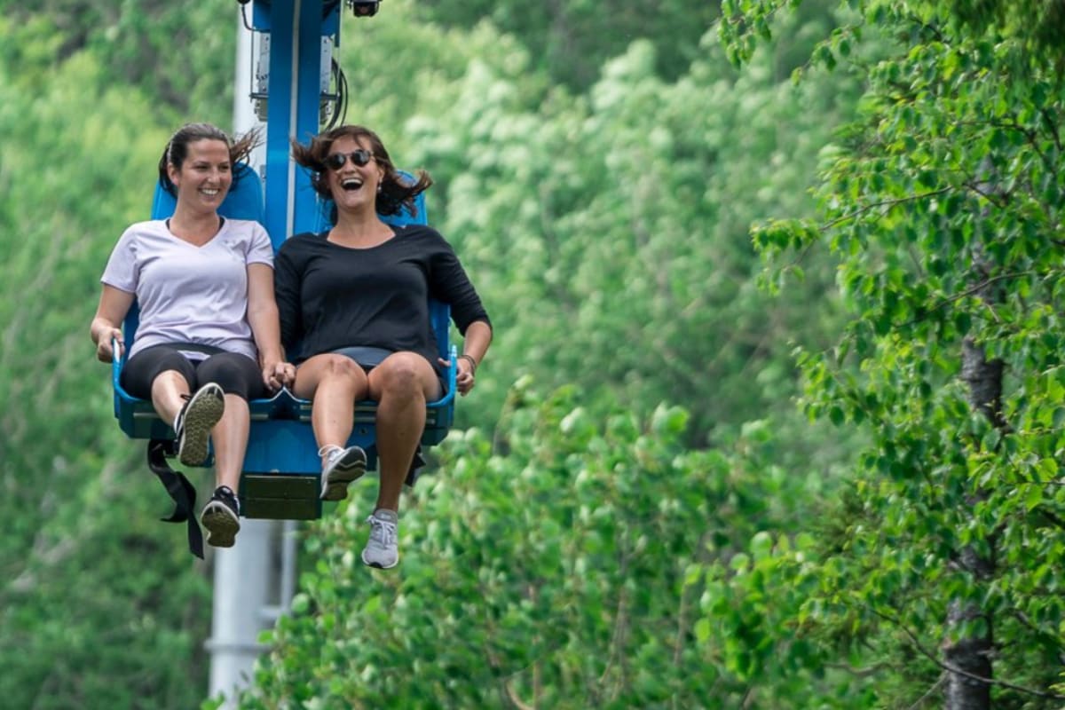 Deux femmes dans un manège aérien au coeur d'une forêt.