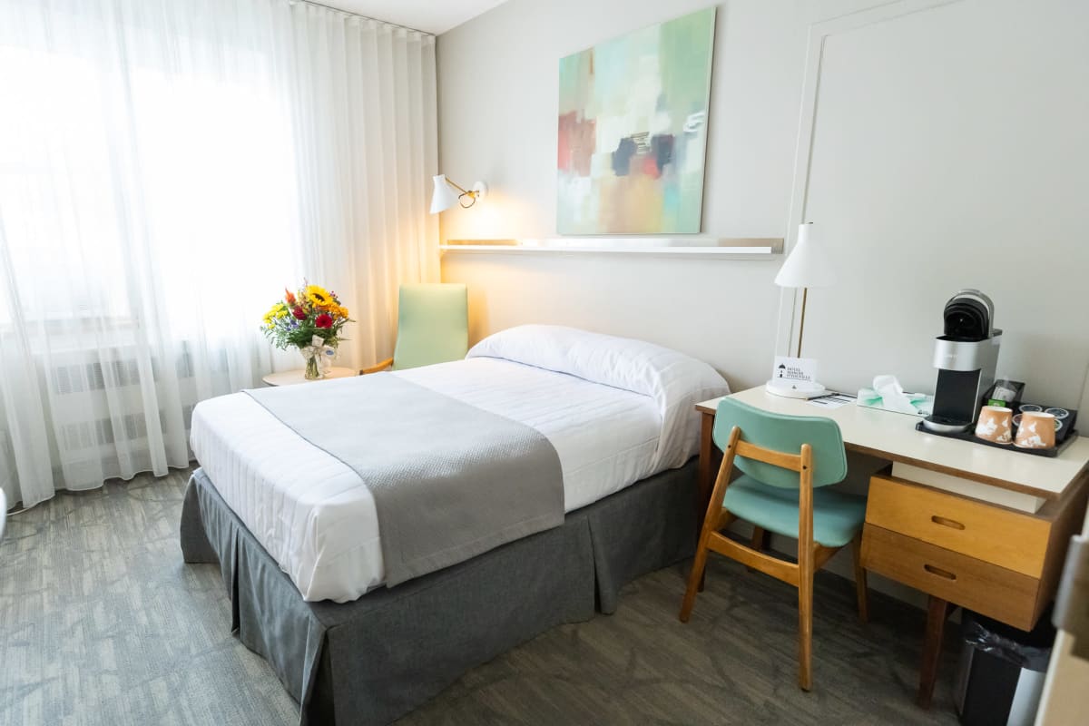 Chambre lumineuse de l'Hôtel Manoir d'Youville avec lit et bureau de travail.