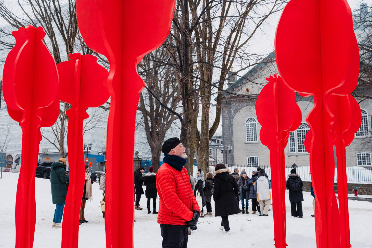 Man looking at an imposing art installation, the red of his coat and the artwork contrasting with the winter landscape.