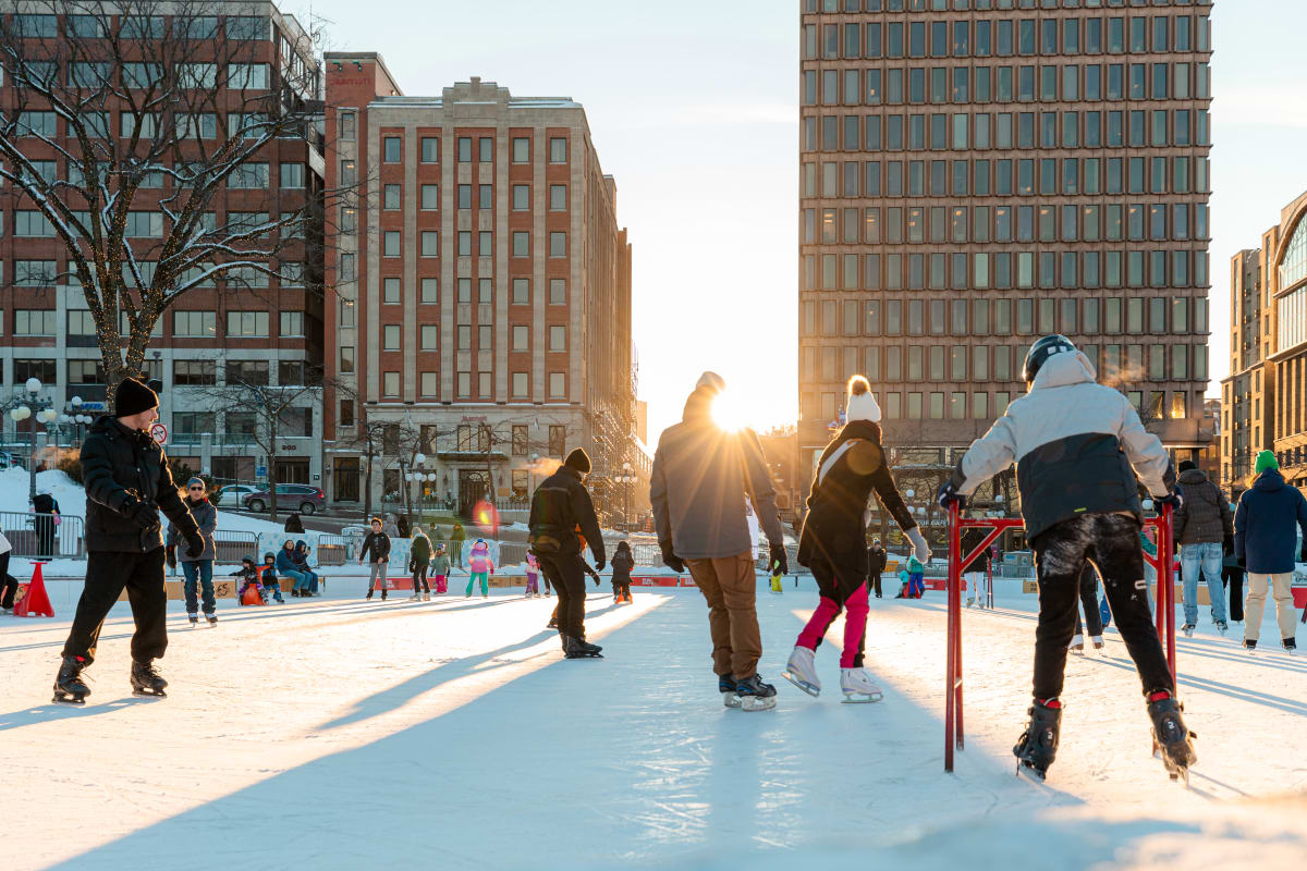 Several people on the ice rink at Place d'Youville as the sun sets on the horizon.